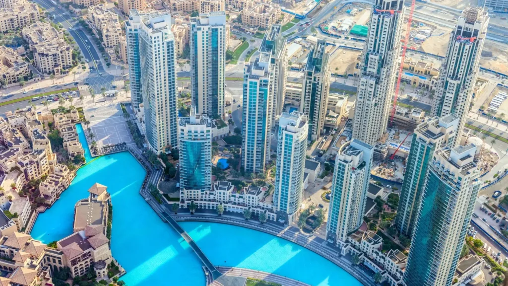 Aerial view of Downtown Dubai with modern high-rise towers around a bright turquoise canal with a bridge and construction nearby