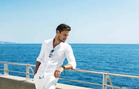 Man in a white shirt leaning on a railing by the ocean under a clear blue sky