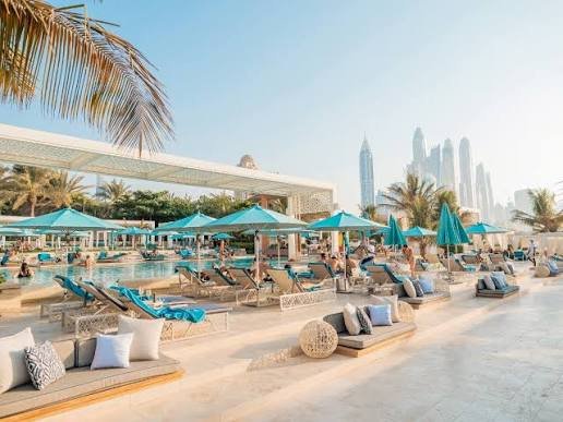 Luxury resort pool deck with turquoise umbrellas, lounge chairs, and a distant city skyline