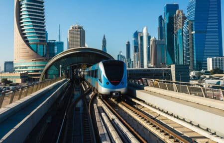 Blue metro train emerging from an elevated station amid a modern skyscraper skyline