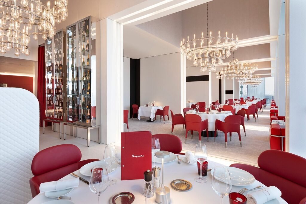 Elegant modern restaurant with red chairs, crystal chandeliers, and white-clothed tables set for dining