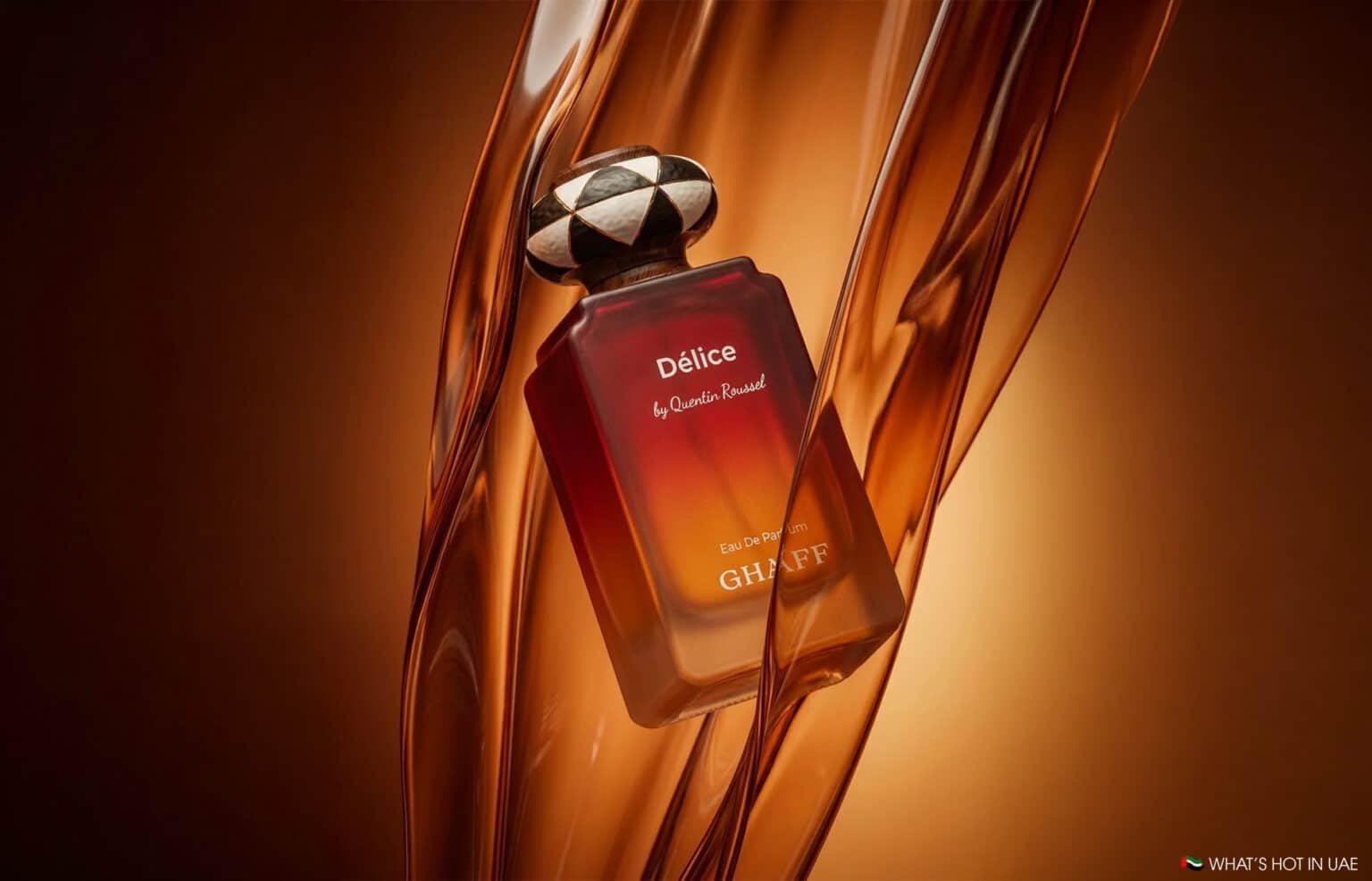 Perfume bottle labeled Délice by Quentin Roussel and GHAFF against flowing amber glass strands