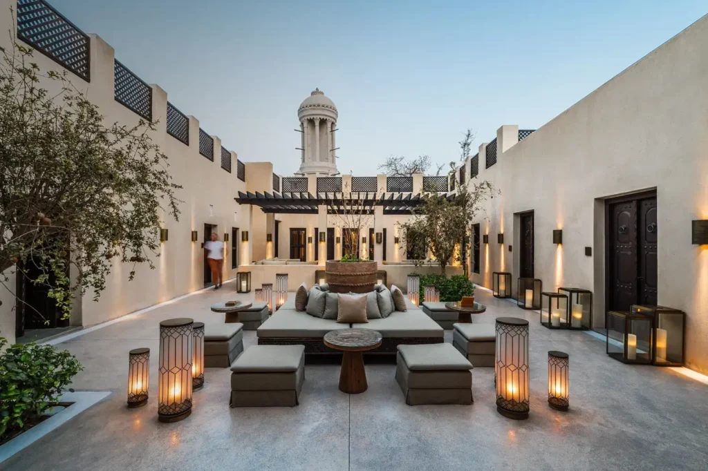 Elegant Sharjah courtyard lounge with low seating, lanterns, and a tower rising above white walls at dusk