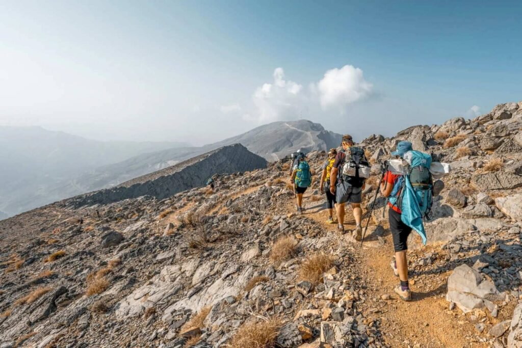 Hikers with backpacks trekking along Jebel Jais mountain trail above a vast valley