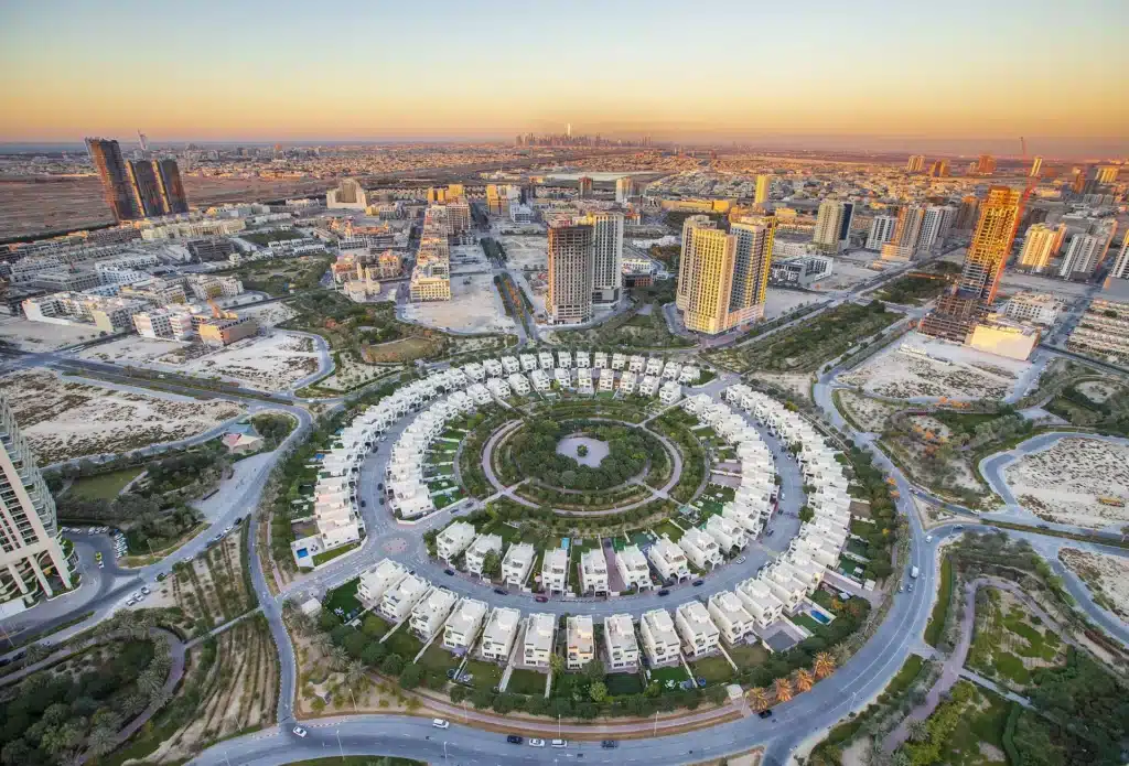 Aerial view of Jumeirah Village Circle amid high-rise towers at sunset, with a distant city skyline