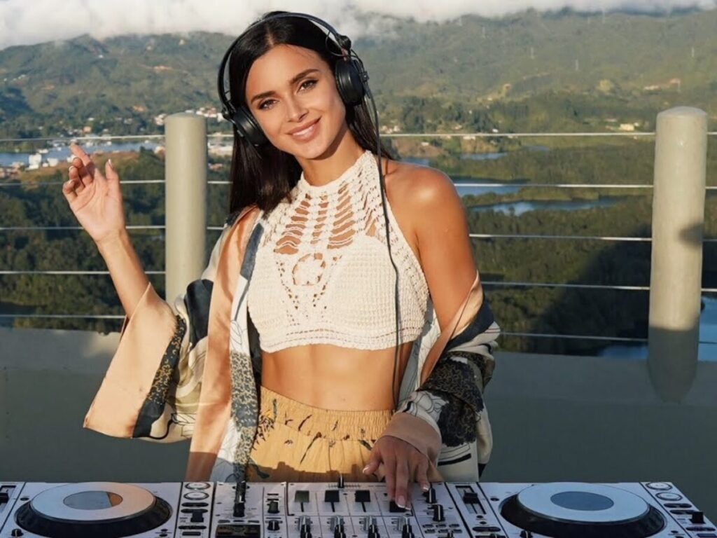 Korolova wearing headphones smiles behind a mixer with mountain views in the background