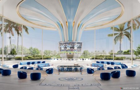 Futuristic lounge with blue seating, a giant central screen, and palm trees visible through glass walls