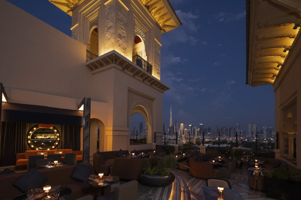 Rooftop lounge with lit Arabian-style arches overlooking a city skyline at dusk