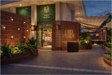 Oro Verde restaurant entrance at dusk with curved wooden walls, tropical plants, and warm lighting