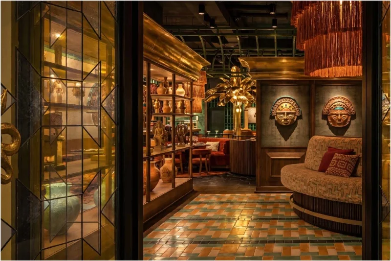 Warmly lit eclectic lounge with mosaic tile floor, carved wall masks, and a curved patterned sofa