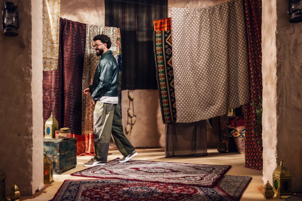 Man smiling in a room filled with hanging patterned rugs and lanterns