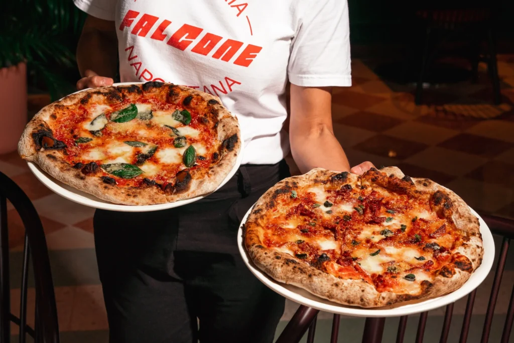 Person holding two large margherita pizzas on white plates in a restaurant