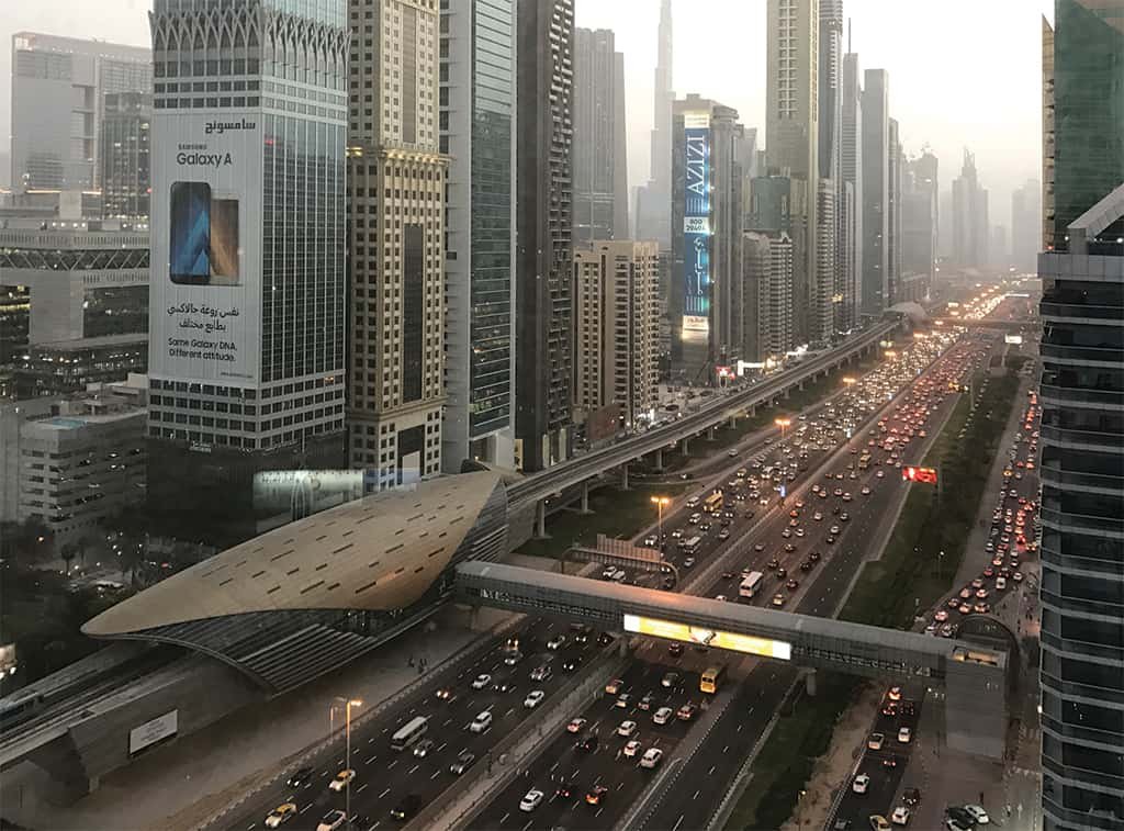 Traffic jam on Sheikh Zayed Road between tall city skyscrapers at dusk with an elevated transit station