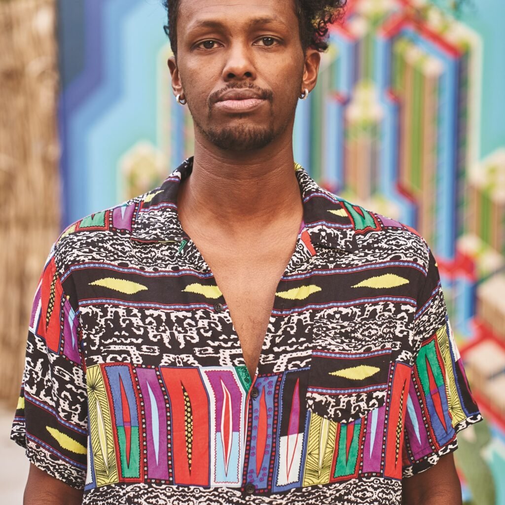 Portrait of Somalie wearing a colorful patterned shirt against a vibrant mural background
