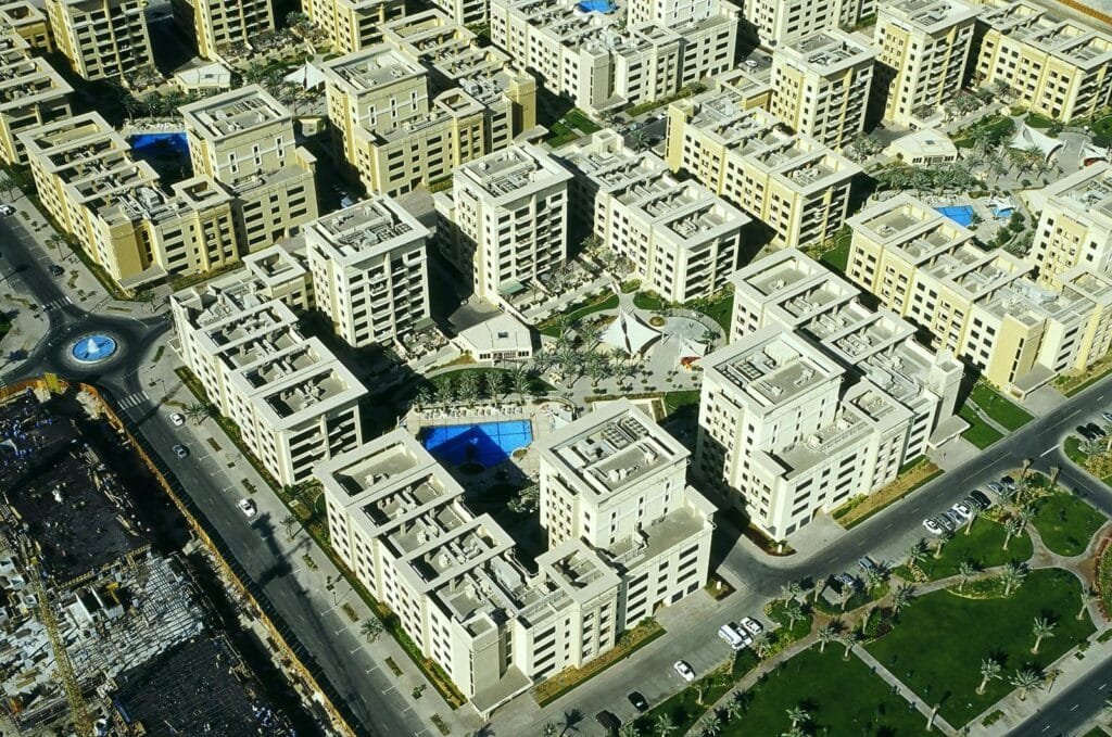 Aerial view of a The Greens residential complex with beige apartment buildings, courtyards, pools, and palm-lined streets