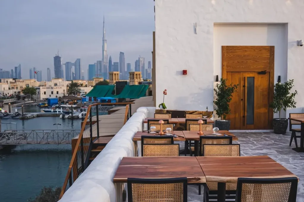 3Fils Dubai Rooftop waterfront restaurant with wooden tables overlooking a marina and a city skyline, including the Burj Khalifa
