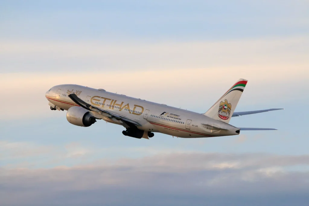 Etihad Airways passenger jet taking off against a pastel sky, with UAE flag colors on its tail