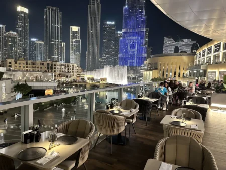 Nighttime rooftop restaurant overlooking Dubai Fountain and illuminated skyscrapers, with diners seated outside