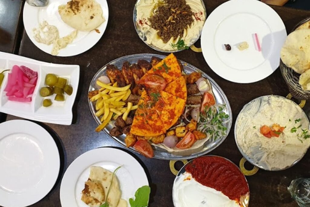 Overhead view of a table spread with grilled meats, fries, flatbread, dips, pickles, and salad