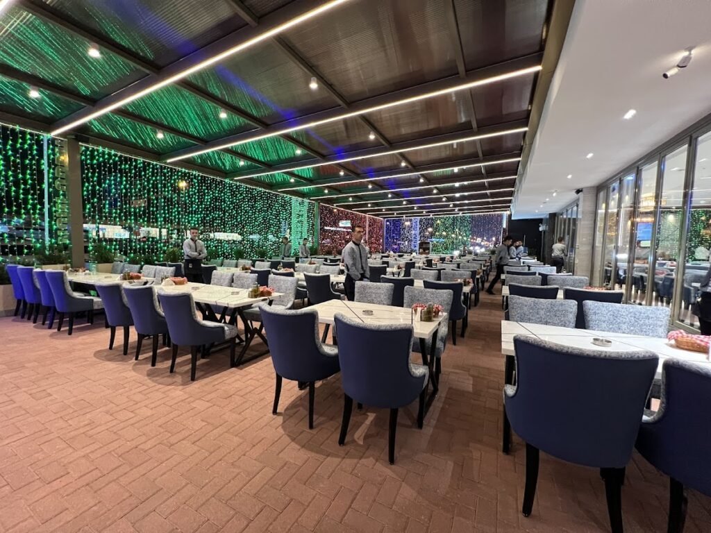 Aroos Damascus Restaurant seating area with neatly set tables, blue chairs, and green string lights along the wall