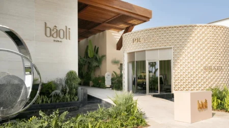 Luxury boutique entrance with Bâoli Dubai and Prada signs, modern cream architecture, and lush landscaping