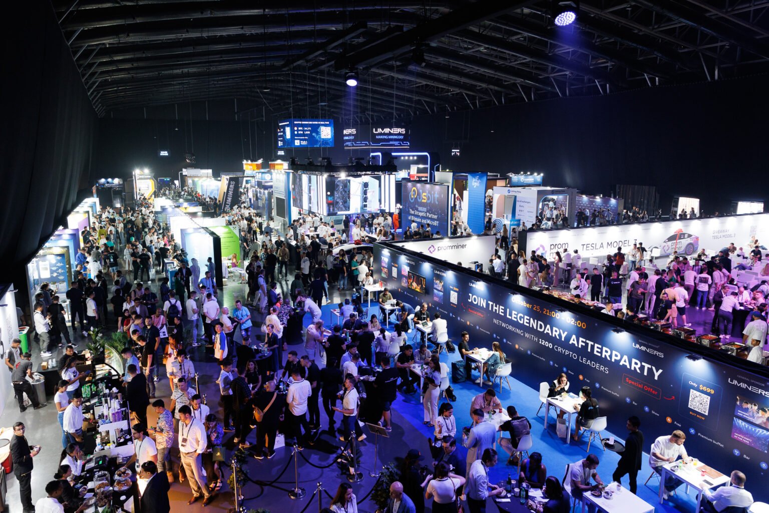 Crowded tech expo hall with glowing booths, large sponsor banners, and attendees networking and eating