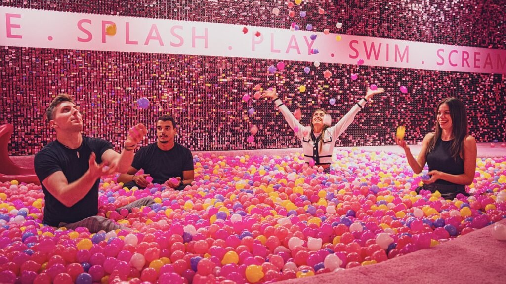 People play in a colorful ball pit while tossing small balloons under a sign that reads SPLASH PLAY SWIM SCREAM