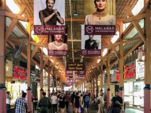 Busy covered market walkway with jewelry shop signs and Malabar Gold & Diamonds banners overhead