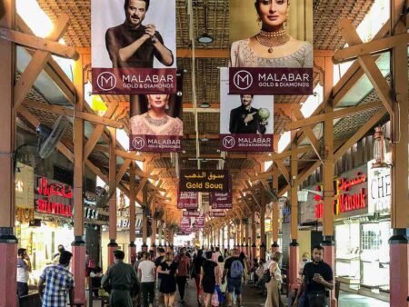 Busy covered market walkway with jewelry shop signs and Malabar Gold & Diamonds banners overhead
