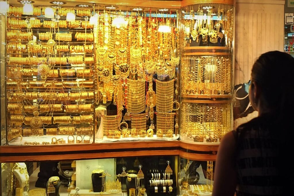 Jewelry shop window filled with gold necklaces, bracelets, and bangles, with a woman looking in from the right