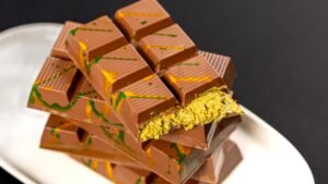 Stacked milk chocolate bars with green and orange swirls, one broken open to reveal pistachio filling