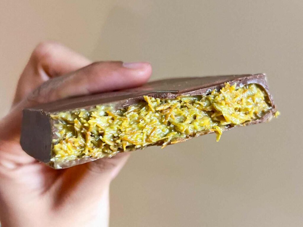 Hand holding a Dubai Chocolate bar with a yellow shredded filling exposed in a cross-section