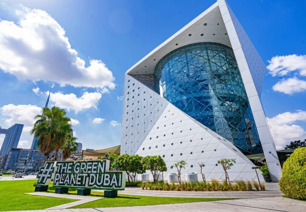 The Green Planet Dubai building with a curved glass facade under a bright blue sky