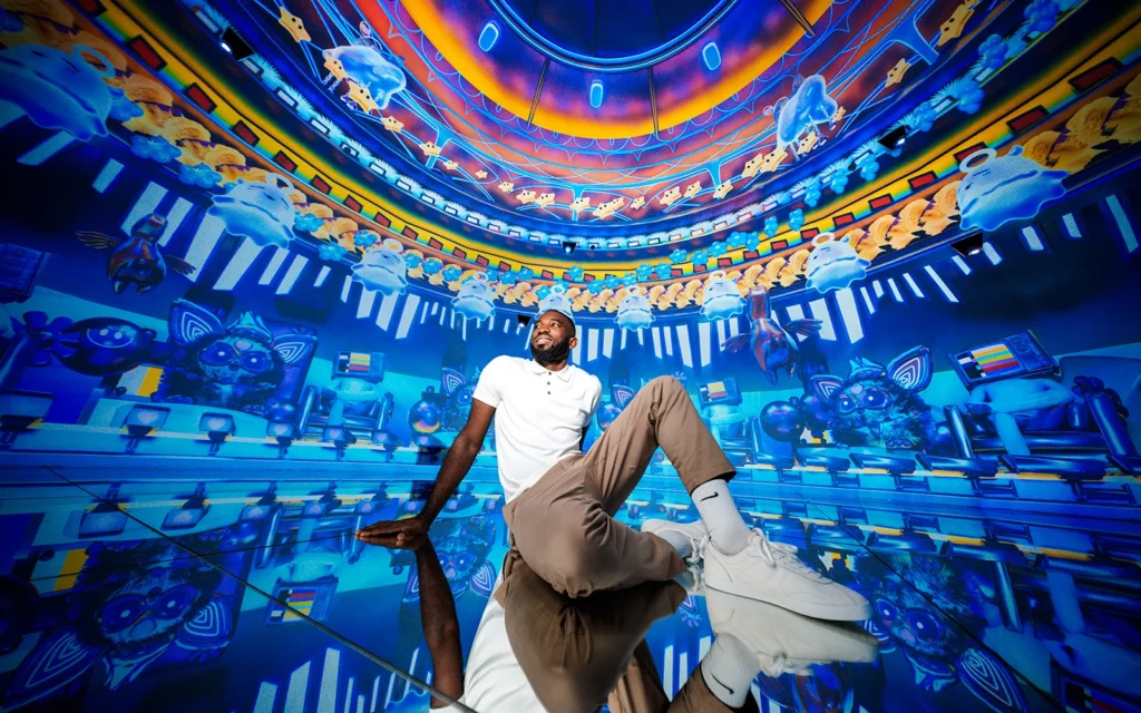 House of Hype Dubai: Everything You Need to Know Man sitting on a reflective floor in a vivid blue and orange digital art installation with cartoon-like floating figures