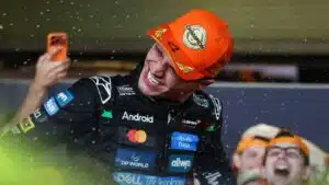 A McLaren Formula 1 driver in a champion’s cap celebrates in the rain as fans take photos