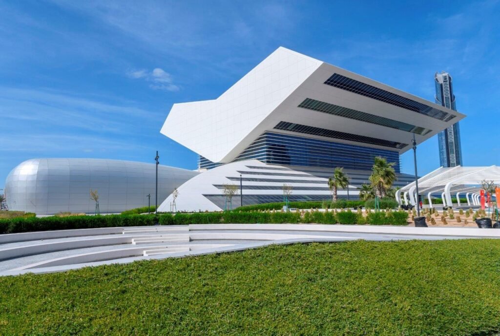 Futuristic white modern building with angular roof and curved silver structures under a blue sky