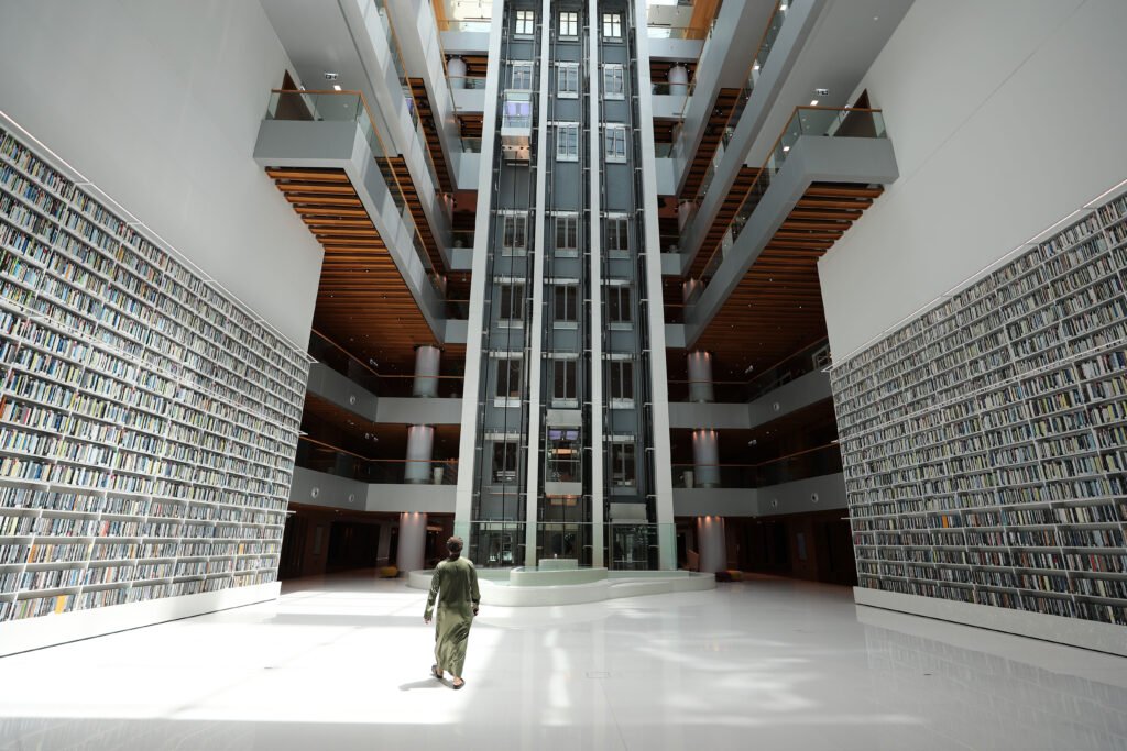 A person walks through Mohammed Bin Rashid Library atrium with towering bookshelves and a central glass elevator