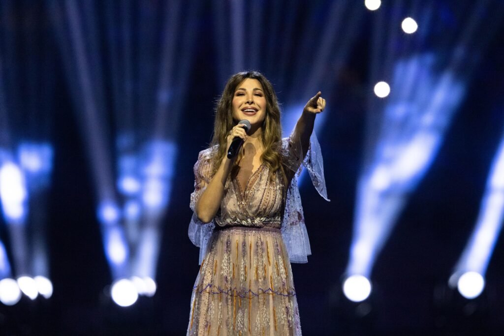 Nancy Ajram to perform live at Coca-Cola Arena in Dubai Singer onstage holding a microphone and pointing toward the audience under blue stage lights