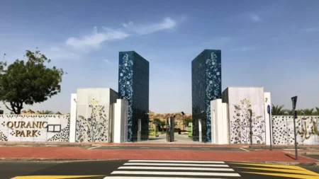 Decorative entrance gate to Quranic Park with floral-patterned towers and a crosswalk in front