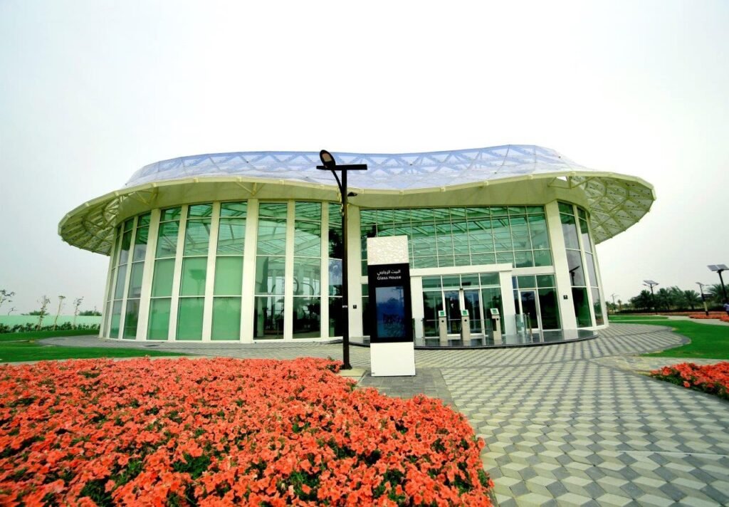 Modern glass visitor center with a curved roof, flower beds, and a paved walkway