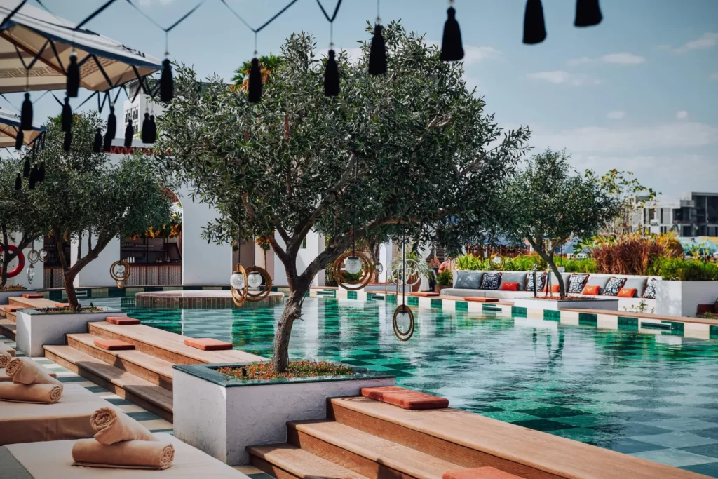 Rooftop pool with trees, lounge seating, and hanging lanterns under a clear sky
