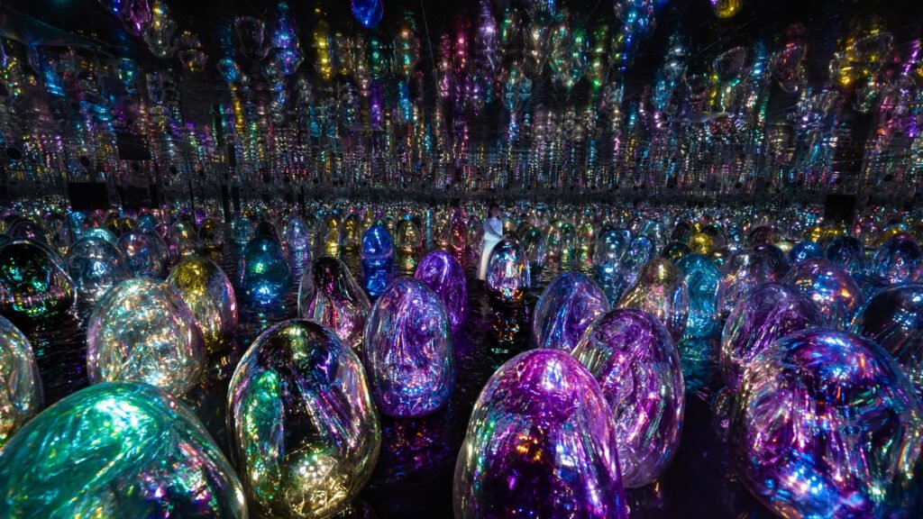 Mirrored room filled with glowing rainbow-colored orb lights and a person standing in the center