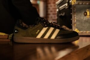 Black and olive Adidas Samba sneaker with cream stripes on a wooden surface