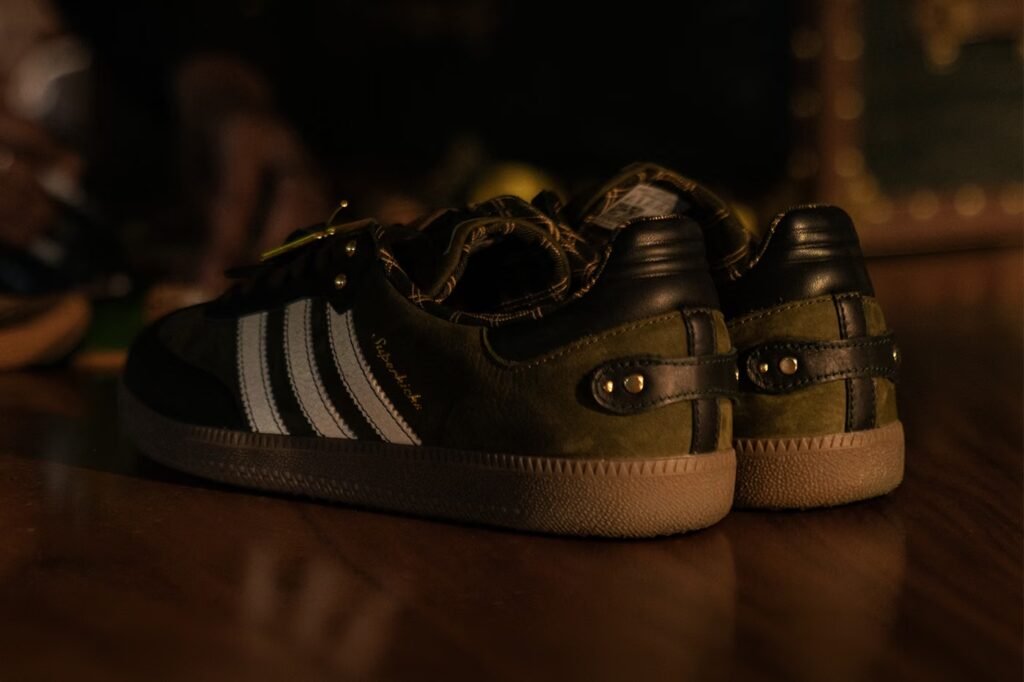 Pair of green and black Adidas sneakers on a wooden floor in dim light
