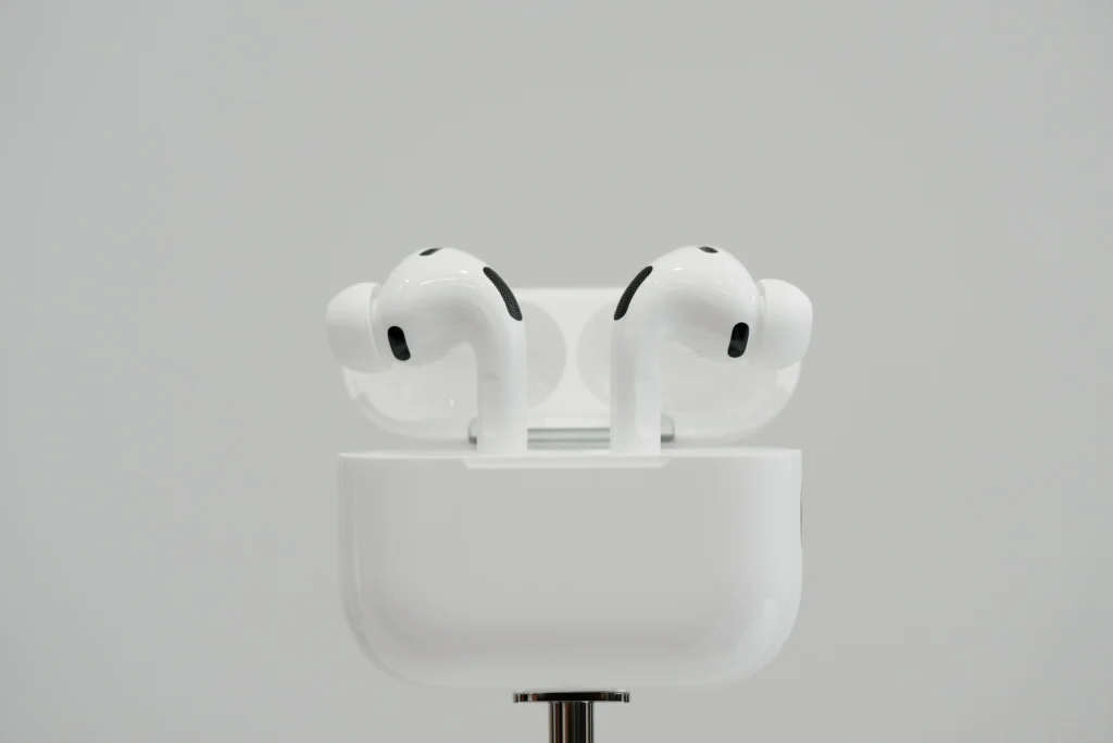 White wireless camera equipped airpods in an open charging case against a plain gray background