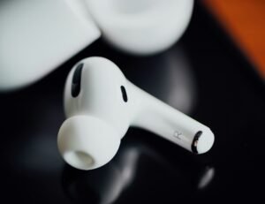 Close-up of a white wireless earbud with silicone tip on a dark reflective surface