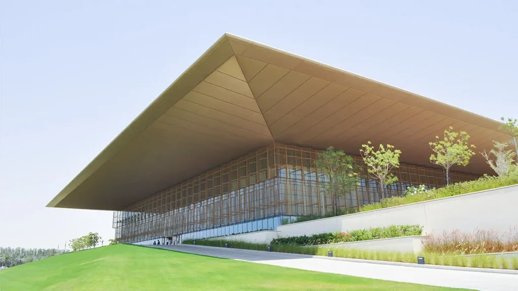 Modern House of Wisdom building with a massive overhanging roof, glass facade, and landscaped green lawn