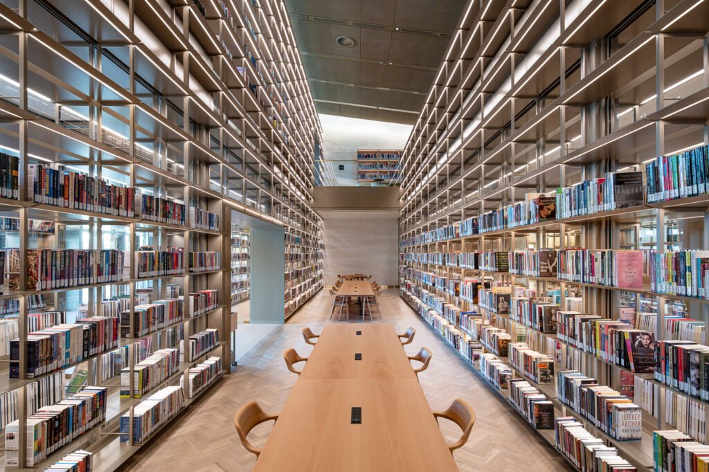 Modern library aisle with tall bookshelves and long wooden study tables