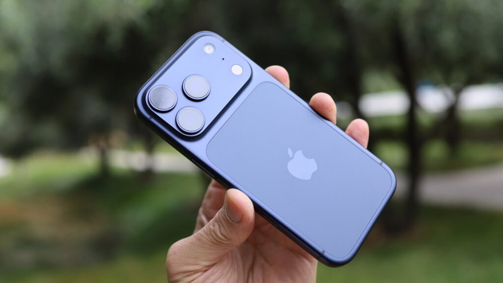 Hand holding a blue iPhone with triple cameras against a blurred green outdoor background