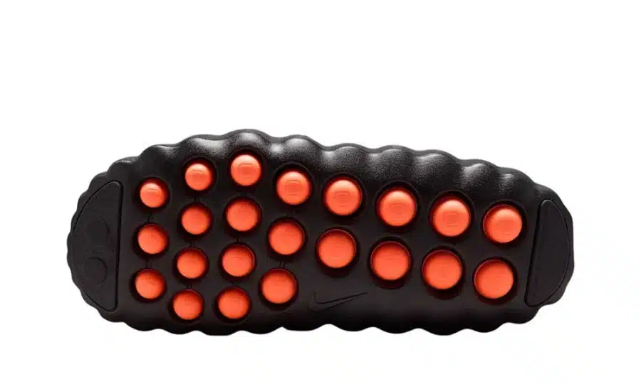 Black textured Nike Mind sole with bright orange traction pods on a white background
